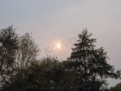 山水太阳摄影照片_奇怪的天空太阳在阴云密布的天空树天际线后面