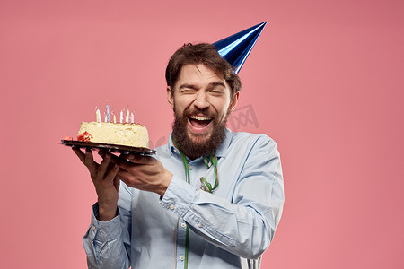 盘子里放着蛋糕、身穿蓝色衬衫、粉红色背景的男人生日假期的裁剪视图