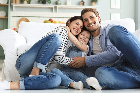 年轻的白人家庭带着小女儿在客厅的地板上放松，微笑的小女孩拥抱父母，表达爱和感激，一起在家休息。