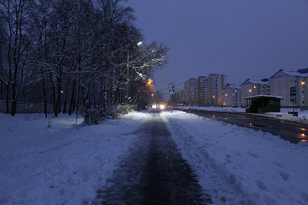 房子和树摄影照片_冬季城市的夜景，晚上在雪地里，靠近房子和灯笼的树灯巷