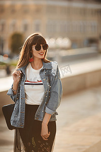 夏日，穿着牛仔夹克和圆形太阳镜在城市街道上行走的年轻嬉皮士女孩