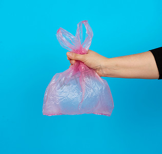 蓝色喜报摄影照片_蓝色背景中手拿着一个空的粉红色塑料袋