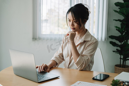 年轻的亚洲女商人坐在前面打开便携式笔记本电脑阅读客户的电子邮件时思考一些事情，长时间的工作概念。