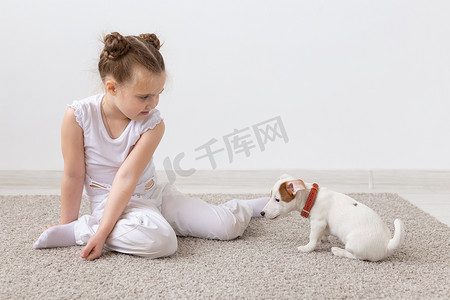 和动物玩耍摄影照片_儿童、宠物和动物概念 — 小女孩在室内与杰克罗素梗小狗玩耍
