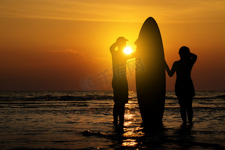 日落时分，男人和女孩在沙滩上拿着冲浪板