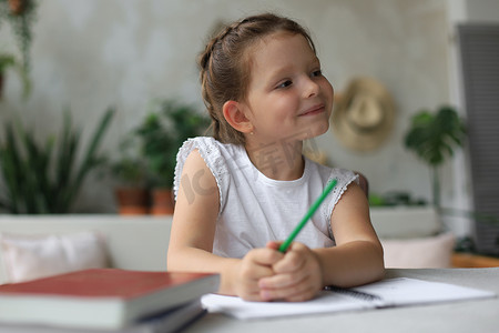 小孩子写字摄影照片_小女孩坐在书桌前，在笔记本上写字，在家做练习，小孩子手写准备作业。