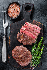 黑色背景摄影照片_菲力牛排里脊肉烤和切片的肉牛排。