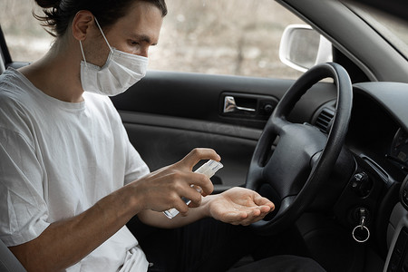 戴防护口罩的男子在计划开车时正在使用防腐剂来保护自己免受细菌病毒的侵害。