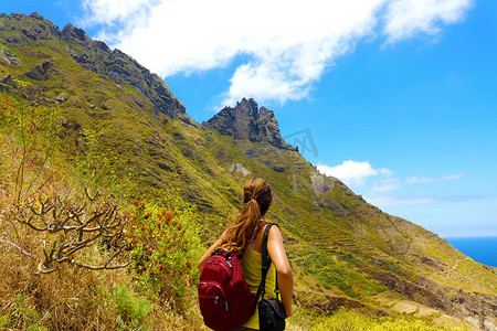 年轻的徒步旅行者女人望着山顶，认为到达山顶需要做很多事情