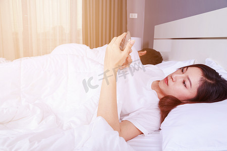 女人在床上玩手机，而她的丈夫睡在她旁边
