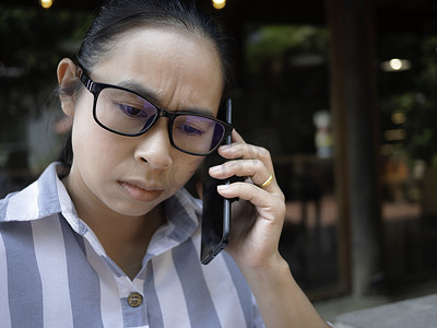压力重重的亚洲年轻女子在咖啡厅打电话。