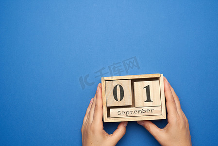 九月日历摄影照片_两只女手拿着一个木制日历，上面写着九月的日期
