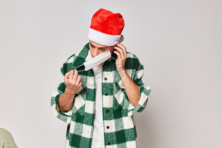 穿格子衬衫的男人摄影照片_穿绿色格子衬衫的男人圣诞老人帽子医疗面罩灰色背景