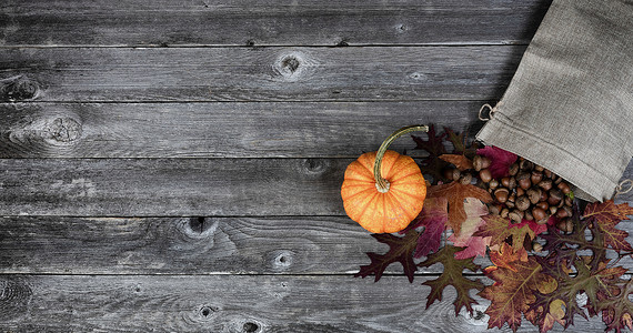秋季系列的质朴木板上装有干叶、橡子和南瓜的粗麻布袋