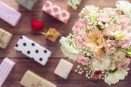 平铺的美丽浪漫鲜花花束，木制背景上有彩色礼盒，顶视图