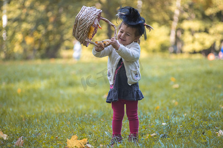 糖果女巫摄影照片_小可爱的女巫在秋天的公园里玩一篮树叶。