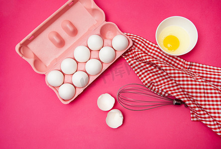 一盒鸡蛋靠近一碗蛋黄，并在粉红色的桌子上搅拌