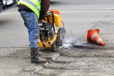 工人在道路施工期间用汽油切割机切割一块劣质沥青。