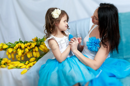 花束妈妈摄影照片_妈妈和女儿坐在沙发上，手里拿着一束鲜花。