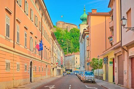 戈里齐亚 — 2020年6月，意大利：一条街道上有鲜艳的橙色建筑、停放的汽车和一个骑自行车的男人