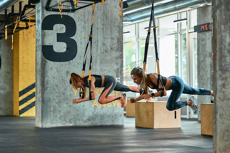 两个年轻的运动女孩在健身房用 trx 健身带锻炼