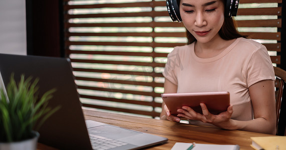 一名亚洲女学生坐在桌边，在家在线学习时使用平板电脑