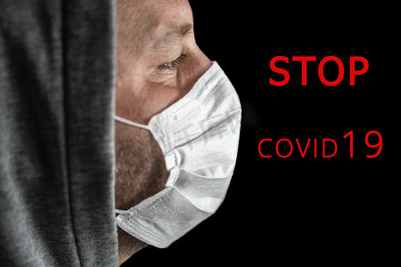 戴着头巾和医用面具的年轻疲惫的男人在黑暗的背景中向前看，红色文字 STOP COVID 19。