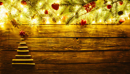 模糊的圣诞背景，有冷杉树枝、干棍圣诞树、仙女灯和棕色木板上的圣诞装饰
