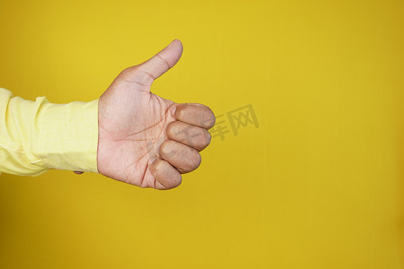 黄色背景下竖起大拇指的男人手