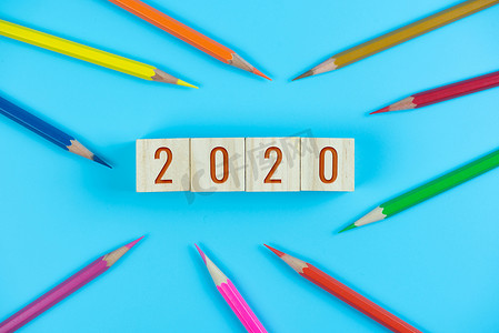 文字2020摄影照片_2020 木立方体上的文字和浅蓝色背景上的彩色铅笔