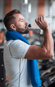 年轻成年男子在健身房的跑步机上喝瓶水。