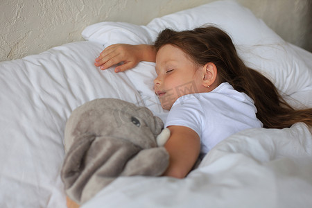 可爱的小女孩和玩具大象一起睡在床上。