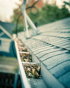 石棉摄影照片_屋顶瓦片附近满是干叶的排水沟，背景是卫星天线