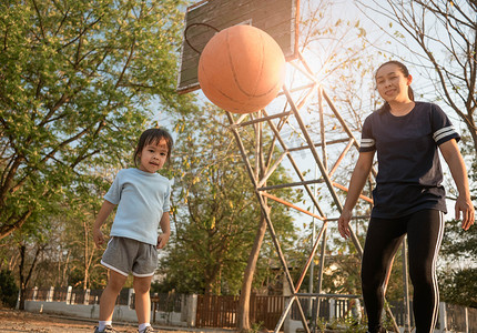 夏日，可爱的亚洲小孩和妈妈在操场上打篮球。