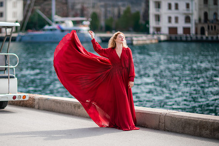 长丝摄影照片_一个穿着红色连衣裙的女人，一个穿着飘逸连衣裙、长着长丝翅膀的时装模特，堤岸上飞扬着织物。