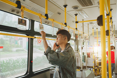 帅气的亚洲男子站在城市公交车上用手机交谈