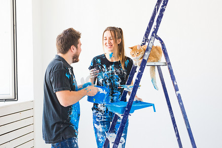 修理、翻新、宠物和情侣概念 — 带猫的年轻家庭一起修理和粉刷墙壁，笑着