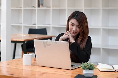 迷人的女人在办公室用笔记本电脑举行视频会议时，通过网络摄像头观看和讲话。