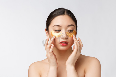 亚洲美女少女用眼下的金色眼罩贴片护理皮肤