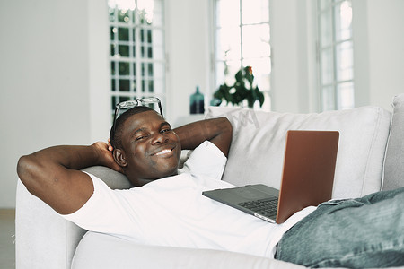 快乐的非洲人，沙发上放着一台笔记本电脑，微笑着