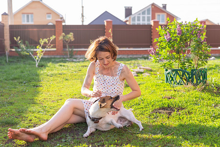在阳光明媚的夏日，积极开朗的女人在她乡间别墅的院子里和她心爱的狗杰克罗素梗犬玩耍。