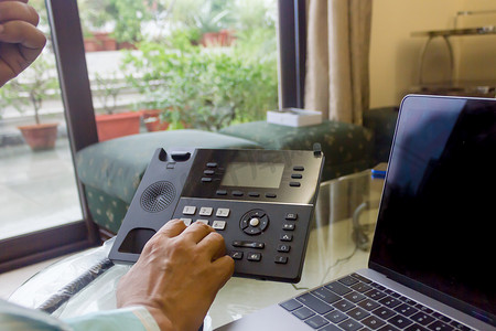 商人在办公室使用台式电脑时拨打固定电话上的电话号码。