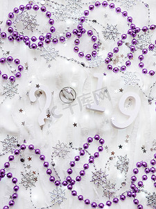圣诞节和新年背景与数字 2019，带钻石的结婚戒指，紫罗兰装饰和灯泡。