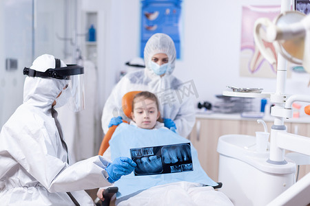 放射防护摄影照片_穿着工作服的牙医穿着个人防护服解释牙科手术