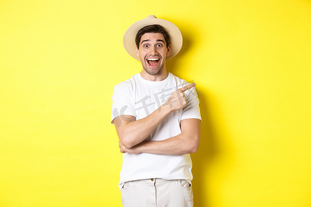 戴草帽的男摄影照片_戴着草帽的快乐男游客向右指着，在复制空间、黄色背景上展示促销优惠