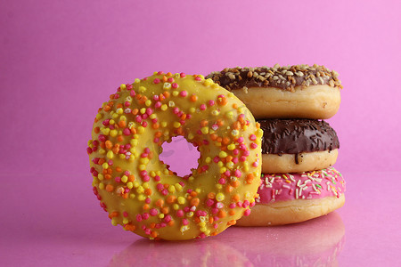 甜蜜的静物甜甜圈柏林特写镜头在后面躺着一堆三个甜甜圈巧克力粉红色黄色在明亮的粉红色紫红色背景上，有一个文本位置和一个 cpixpe 用于咖啡馆的桌布胶水