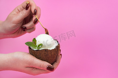 新鲜椰子一半的香草冰淇淋球，手上装饰着薄荷叶，粉色背景上有勺子