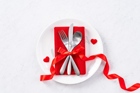 盘子套装摄影照片_情人节膳食设计理念-浪漫的盘子套装隔离在大理石白色背景上，用于餐厅节日庆典促销、顶视图、平躺。