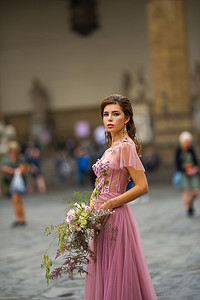 女孩捧花摄影照片_意大利佛罗伦萨老城中心，身穿粉色连衣裙、捧花的新娘站立