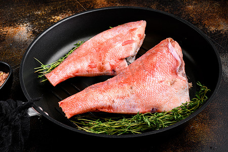深色餐桌背景摄影照片_红海鲈鱼生鱼片，在煎铸铁锅中，在旧的深色乡村餐桌背景上